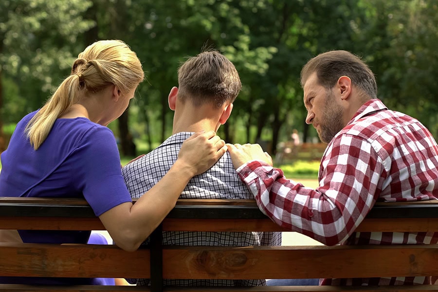 Inclusive self-harm support, parents gently reassuring a young person on a park bench