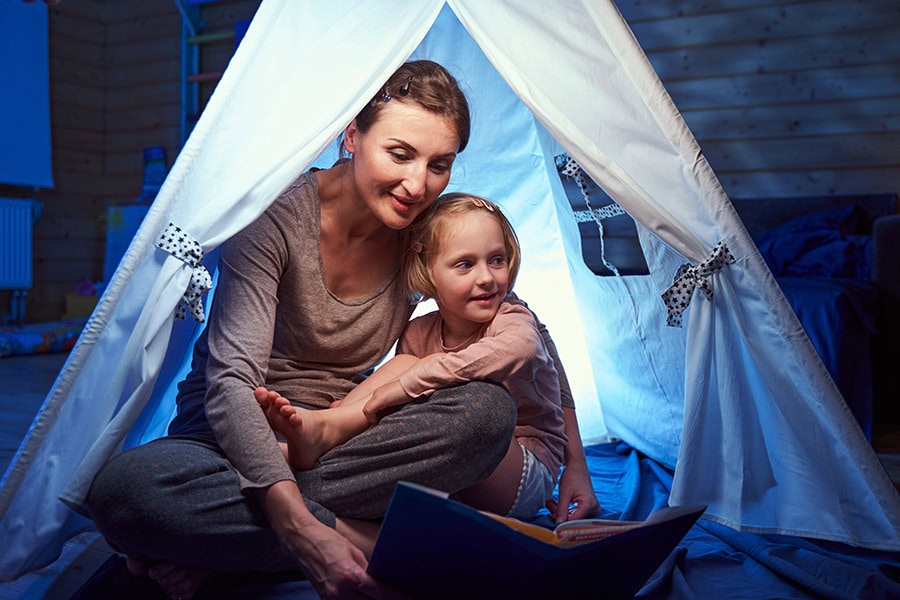 Mother and young child sitting in an indoor tent reading together while the parent calmly explains storms, thunder and lightning in simple language.