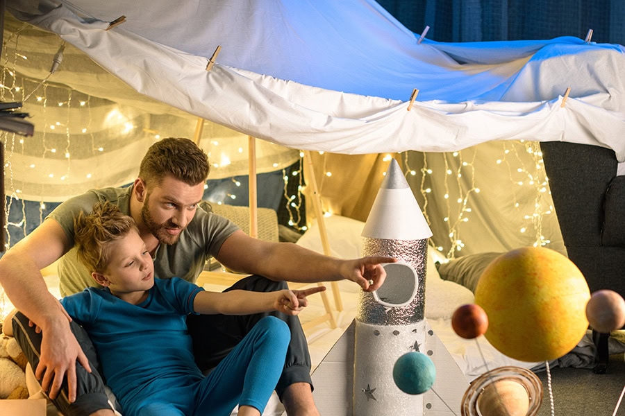 Parent and child sitting in a cosy blanket fort at home, creating a storm safe space to help with storm anxiety in children